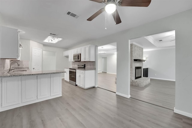 kitchen featuring visible vents, light stone countertops, stainless steel appliances, a brick fireplace, and a sink