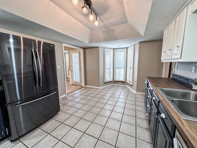 kitchen featuring light tile patterned floors, a raised ceiling, freestanding refrigerator, a textured ceiling, and backsplash