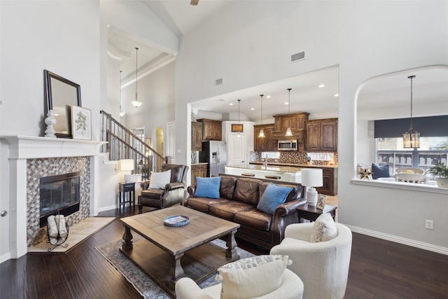 living room with visible vents, wood finished floors, high vaulted ceiling, a tile fireplace, and baseboards