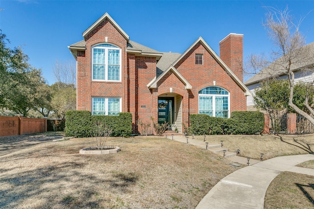 traditional home with a front yard, a chimney, fence, and brick siding