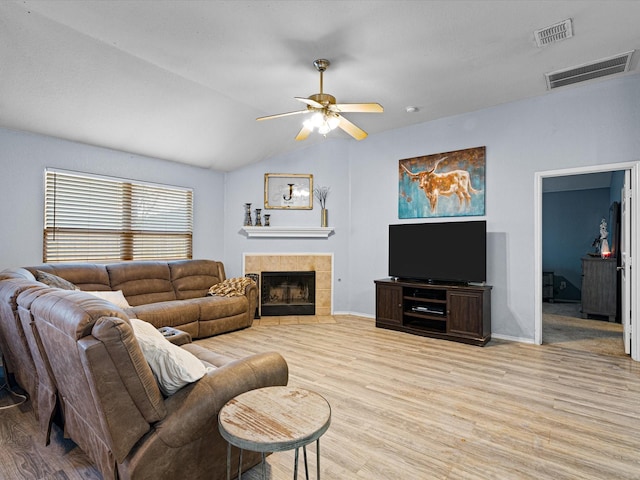 living room featuring light wood-style floors, a tile fireplace, visible vents, and lofted ceiling