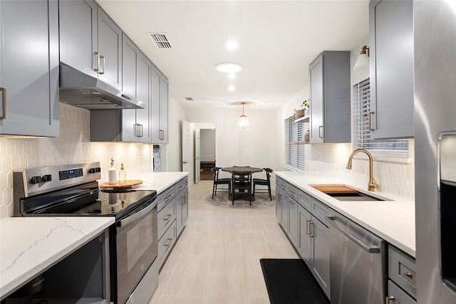 kitchen with under cabinet range hood, stainless steel appliances, a sink, visible vents, and gray cabinets