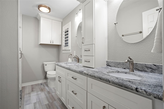 full bath with toilet, double vanity, baseboards, and a sink