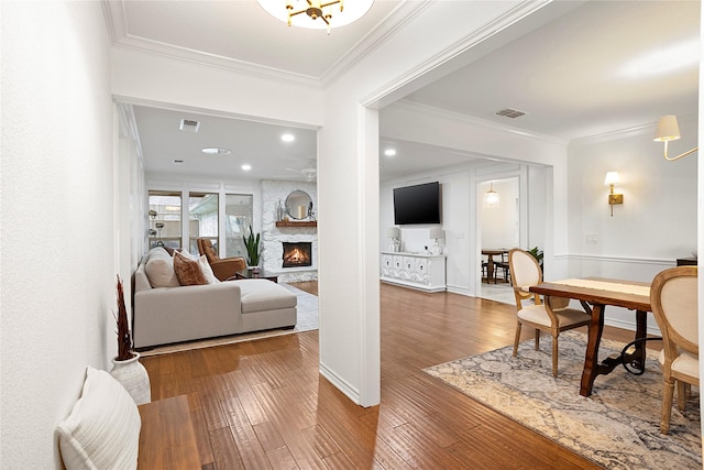 living area with a stone fireplace, wood-type flooring, visible vents, and crown molding