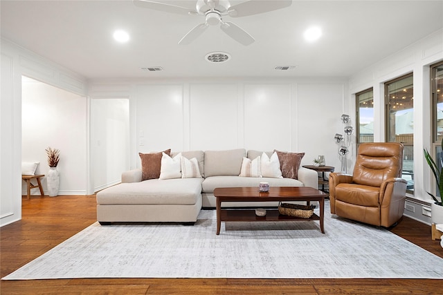 living room with ceiling fan, visible vents, a decorative wall, and wood finished floors