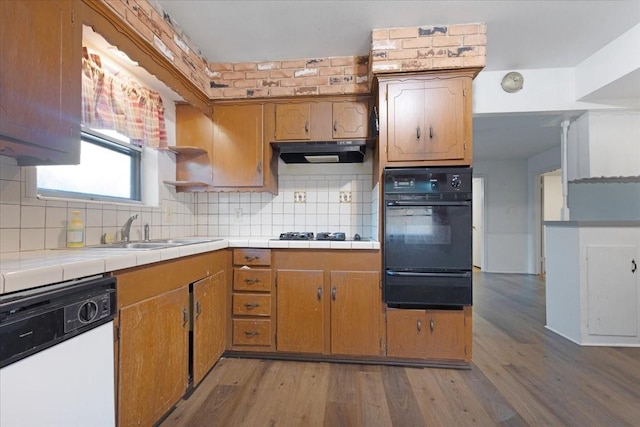 kitchen featuring tile countertops, under cabinet range hood, black appliances, a sink, and a warming drawer