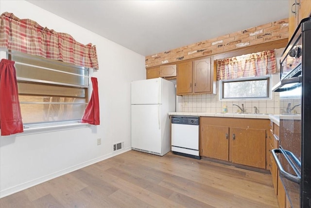 kitchen featuring white appliances, tasteful backsplash, light wood finished floors, visible vents, and a sink