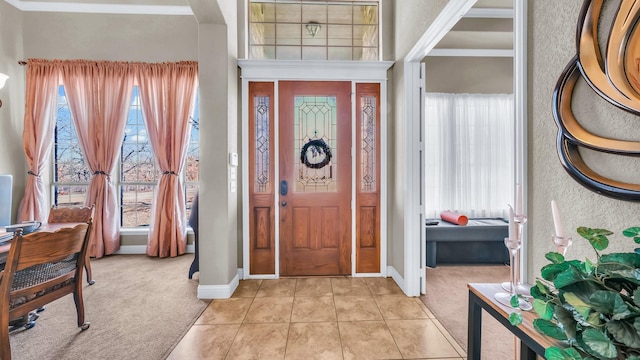 foyer entrance featuring light carpet, light tile patterned floors, baseboards, and crown molding