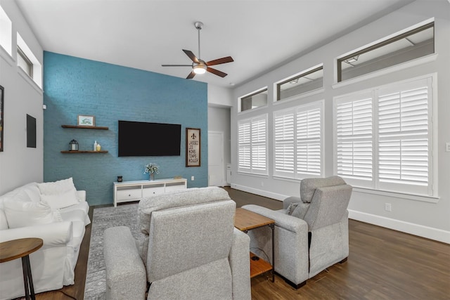 living room with an accent wall, a ceiling fan, baseboards, and wood finished floors