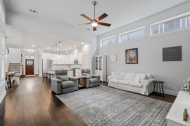 living area featuring stairs, dark wood-style flooring, plenty of natural light, and visible vents