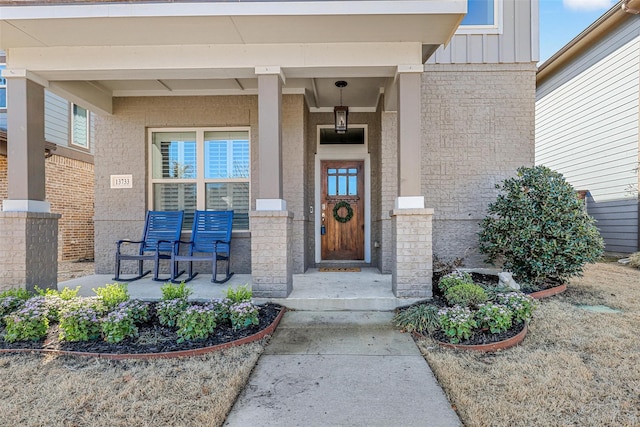 doorway to property with a porch, board and batten siding, and brick siding