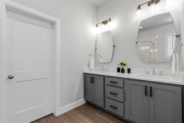 full bathroom featuring double vanity, baseboards, a tile shower, and a sink