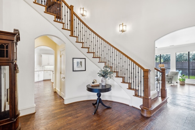 staircase with a towering ceiling, baseboards, arched walkways, and wood finished floors