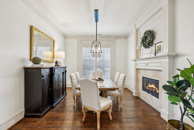 dining space with ornamental molding, dark wood finished floors, a tiled fireplace, and a chandelier