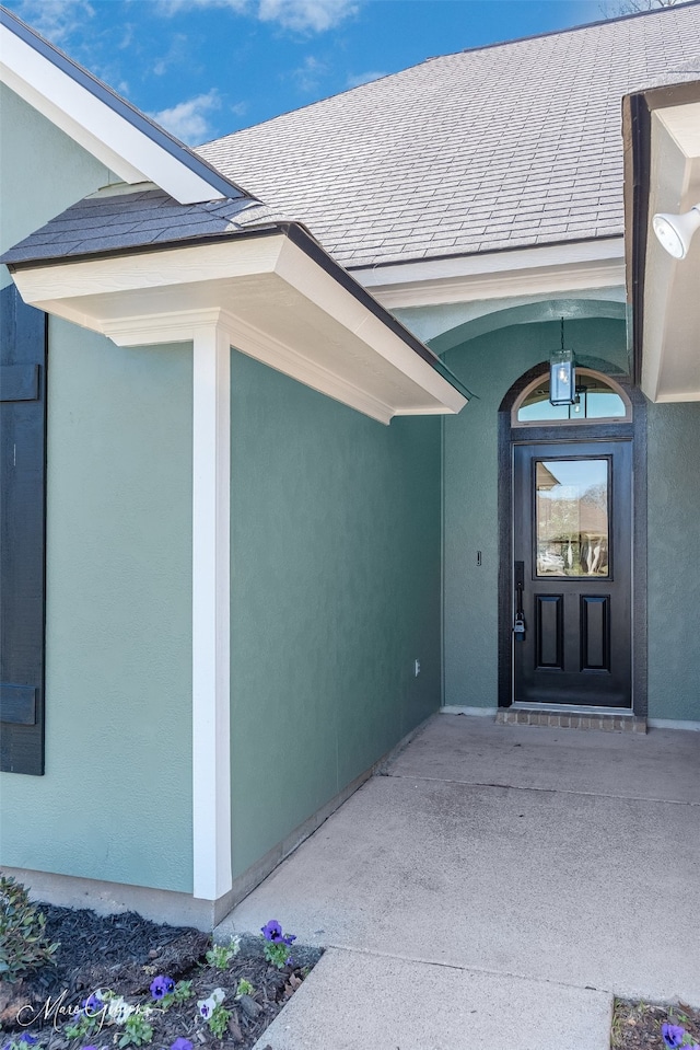 entrance to property with a shingled roof and stucco siding