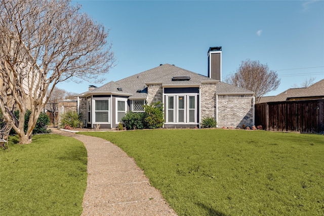 rear view of property with brick siding, a shingled roof, fence, a yard, and a chimney