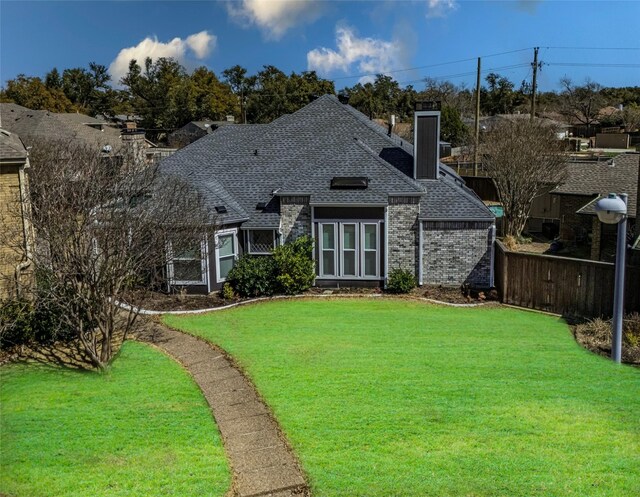 back of property with brick siding, a shingled roof, fence, a yard, and a chimney