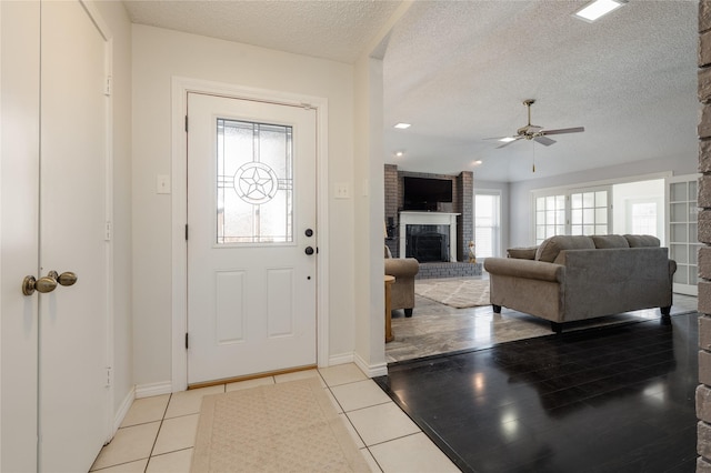 entrance foyer with a brick fireplace, light tile patterned floors, a ceiling fan, and a textured ceiling