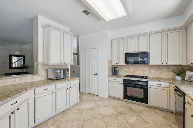 kitchen with a toaster, visible vents, decorative backsplash, light stone counters, and black appliances