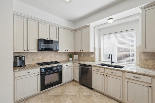 kitchen with light tile patterned floors, cream cabinets, a sink, black appliances, and tasteful backsplash