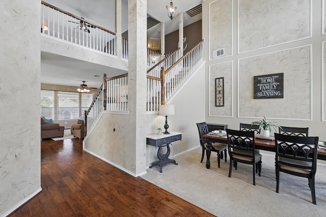 dining room with visible vents, baseboards, hardwood / wood-style flooring, stairs, and a high ceiling