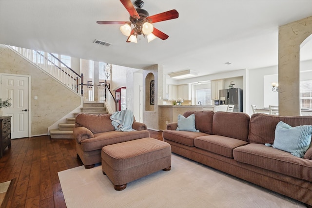 living area with arched walkways, visible vents, stairway, a ceiling fan, and hardwood / wood-style floors