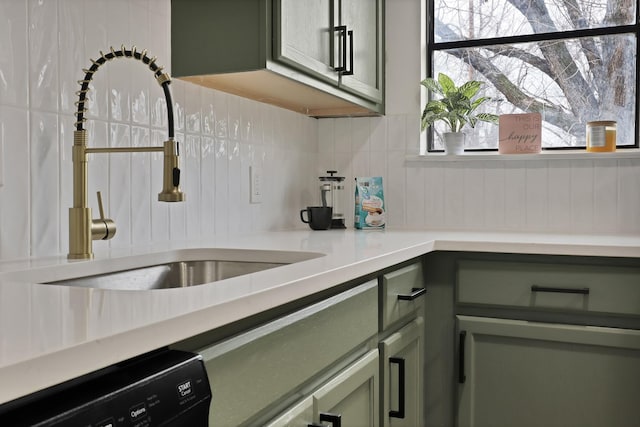 kitchen with tasteful backsplash, green cabinetry, dishwashing machine, light countertops, and a sink