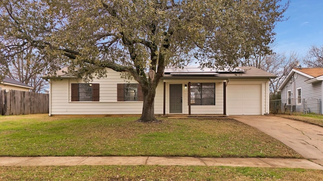 ranch-style house featuring concrete driveway, an attached garage, fence, roof mounted solar panels, and a front lawn