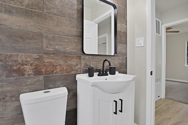 half bath with tile walls, vanity, toilet, and wood finished floors