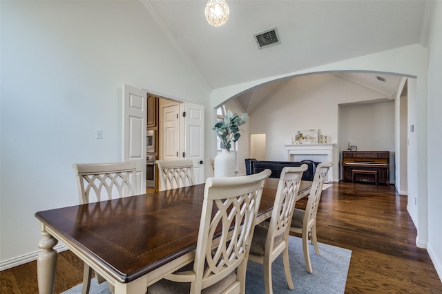 dining area with arched walkways, a fireplace, visible vents, dark wood-type flooring, and vaulted ceiling