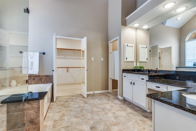 full bathroom featuring a garden tub, vanity, a towering ceiling, and a spacious closet