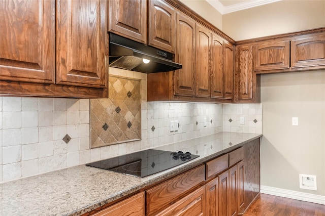 kitchen with crown molding, light stone countertops, under cabinet range hood, baseboards, and black electric cooktop