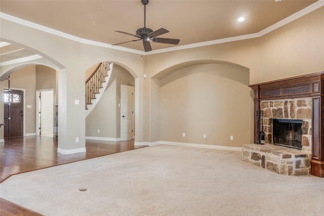 unfurnished living room with baseboards, ornamental molding, arched walkways, and a stone fireplace