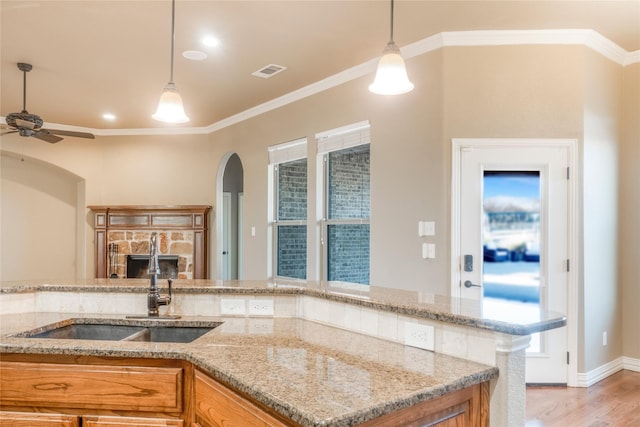 kitchen featuring visible vents, brown cabinets, crown molding, light wood-type flooring, and a sink