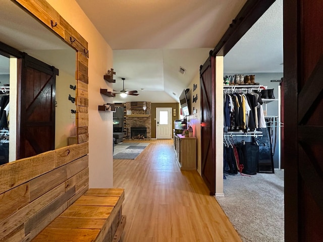 hallway featuring a barn door, visible vents, vaulted ceiling, and wood finished floors