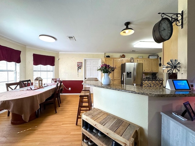 kitchen featuring a peninsula, stainless steel fridge with ice dispenser, light wood finished floors, dark stone countertops, and crown molding