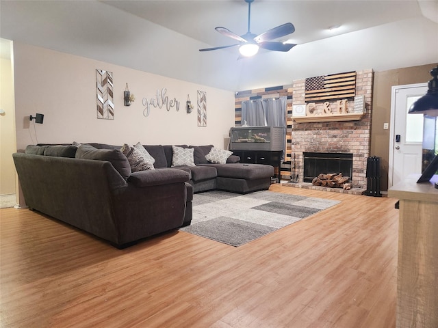 living area featuring lofted ceiling, a fireplace, wood finished floors, and a ceiling fan