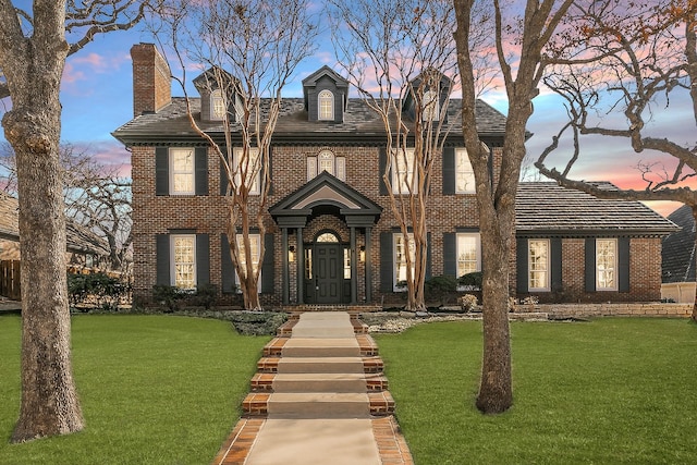 georgian-style home featuring a chimney, a front lawn, and brick siding