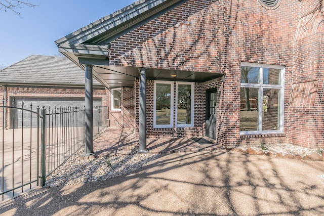 doorway to property with a garage, driveway, fence, and brick siding