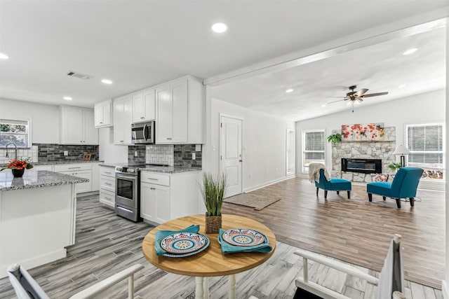 kitchen featuring visible vents, white cabinets, stainless steel appliances, a stone fireplace, and light wood-style floors