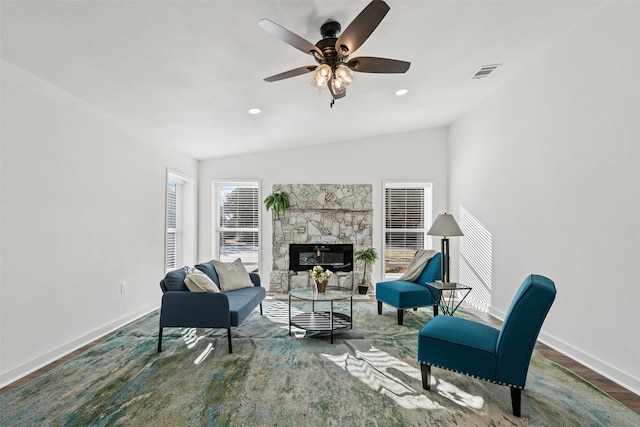 living area with visible vents, a ceiling fan, a glass covered fireplace, vaulted ceiling, and baseboards