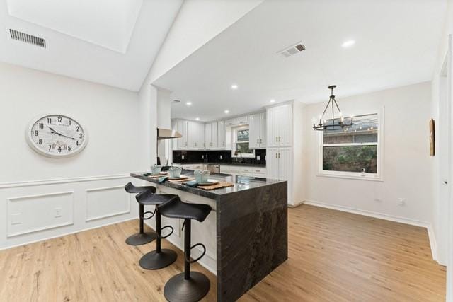 kitchen with dark countertops, visible vents, under cabinet range hood, and a kitchen breakfast bar