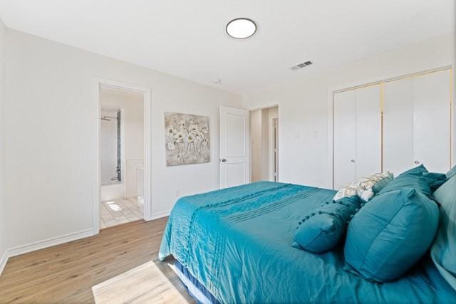 bedroom featuring baseboards, visible vents, connected bathroom, wood finished floors, and a closet