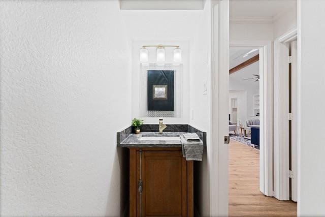 bathroom with a textured wall, vanity, crown molding, and wood finished floors