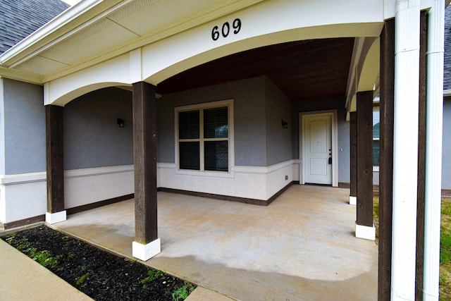 view of exterior entry featuring roof with shingles and stucco siding