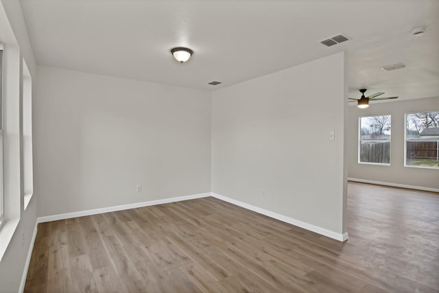 spare room featuring a ceiling fan, visible vents, baseboards, and wood finished floors