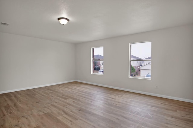 empty room with light wood-style floors, visible vents, and baseboards