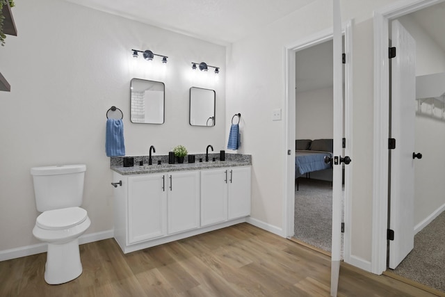 bathroom with ensuite bathroom, toilet, a sink, wood finished floors, and double vanity