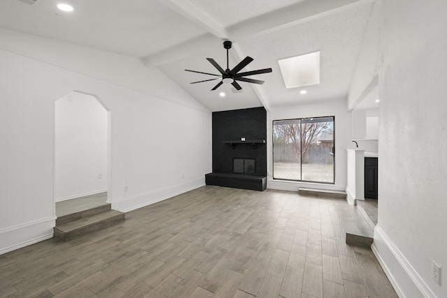 unfurnished living room featuring arched walkways, ceiling fan, a fireplace, and wood finished floors