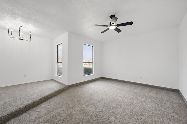 empty room with carpet flooring, a textured ceiling, baseboards, and ceiling fan with notable chandelier